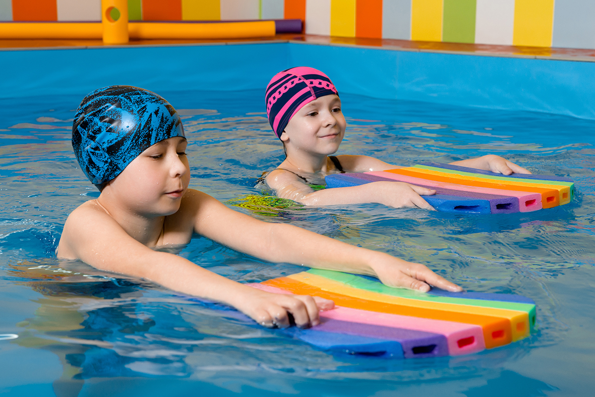 Boy and girl wearing swimsuit uses a foam pad to practice swimming in swimming pool